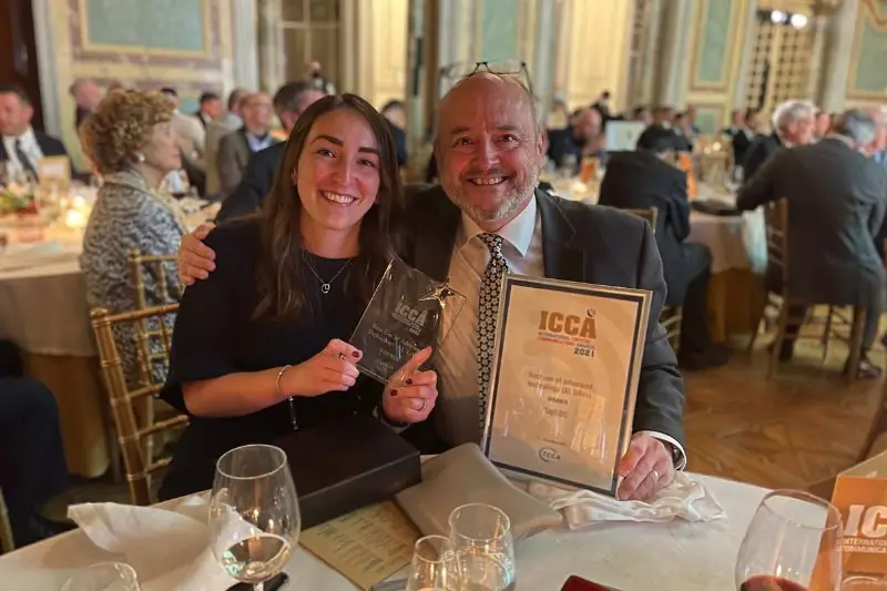 Two people at an awards dinner table with an ICCA trophy and certificate