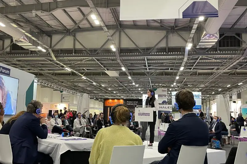 A talk to a seated audience in a busy exhibition hall
