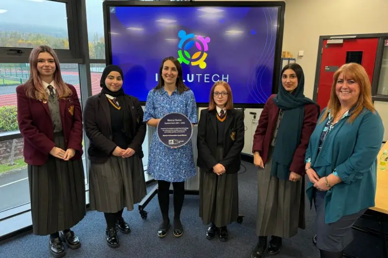 A school visit, with pupils and staff in front of an Inclutech presentation and a commemorative plaque
