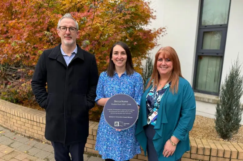Three people outdoors, one holding a commemorative plaque