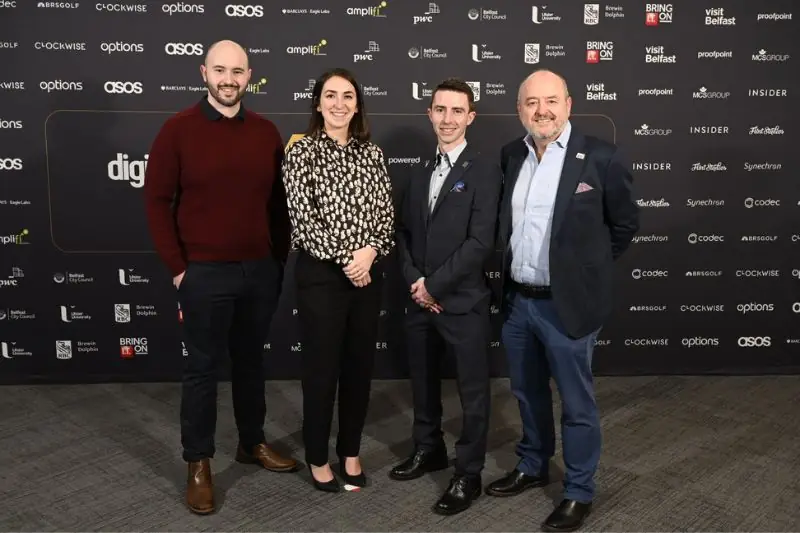 Four people at a digital awards event in front of a sponsor wall