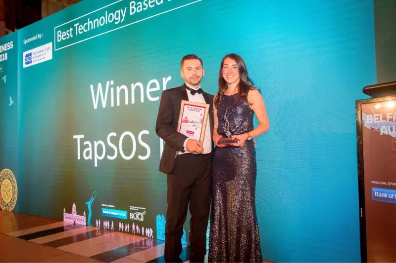 Two people on stage in front of a screen reading Winner TapSOS